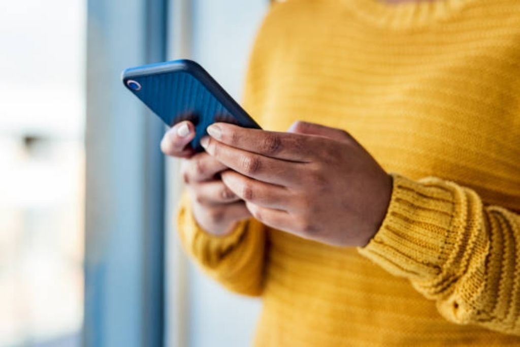 Close up of a person wearing a yellow sweater holding a cell phone