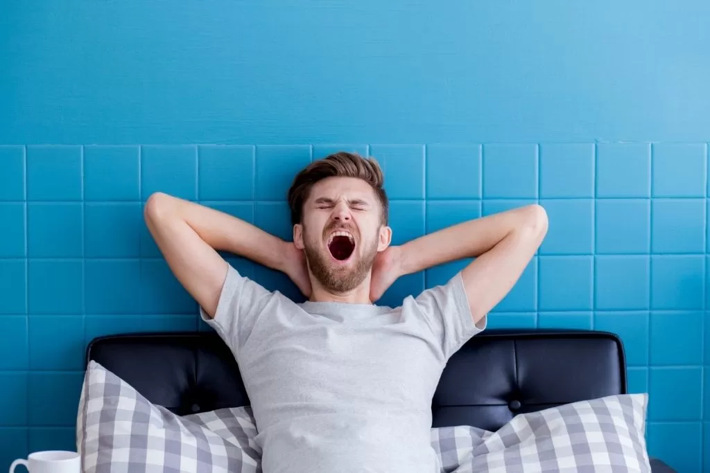 Man sitting up in bed, yawning and stretching