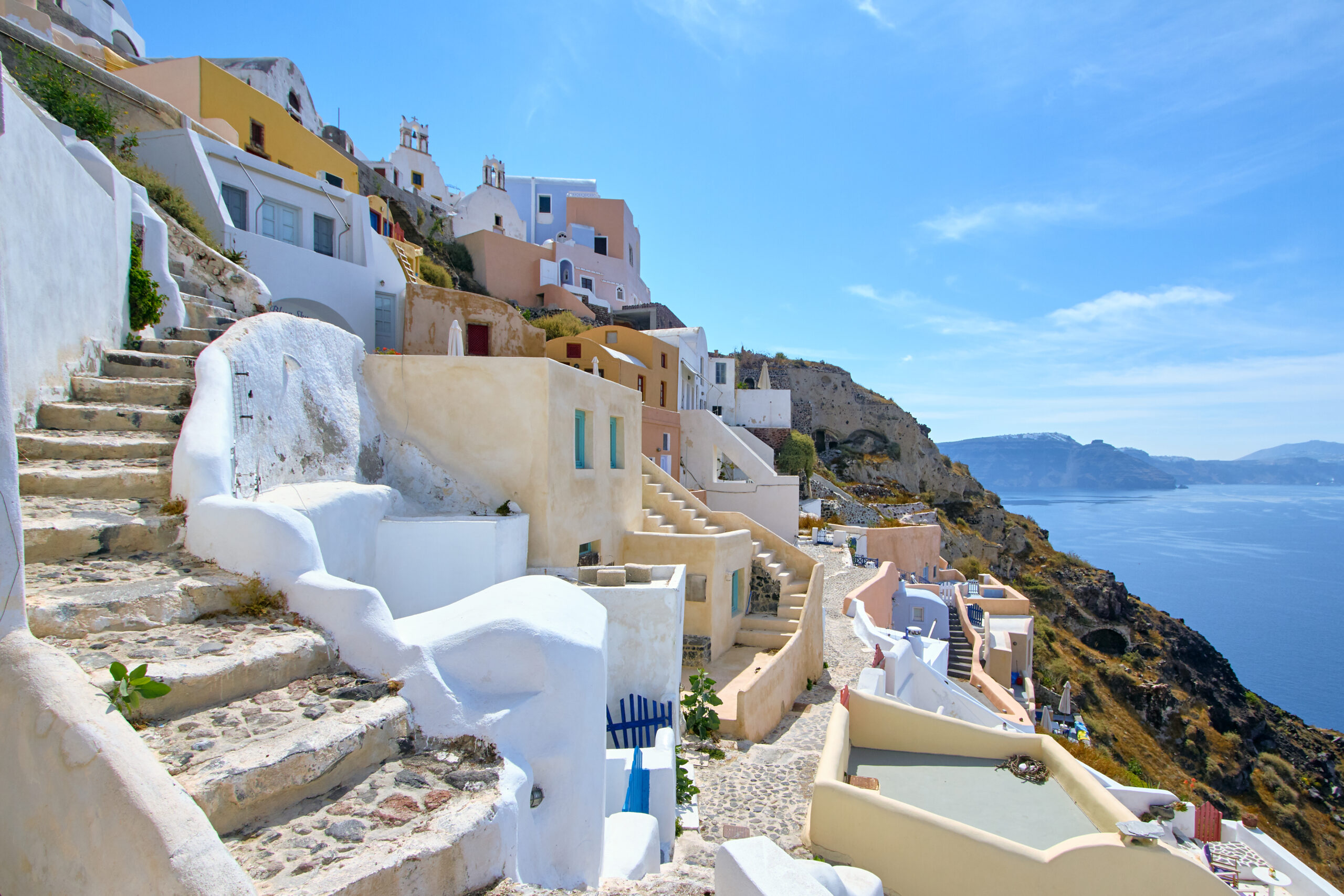 White stucco buildings lining a seaside cliff in Greece overlooking the blue Mediterranean Sea