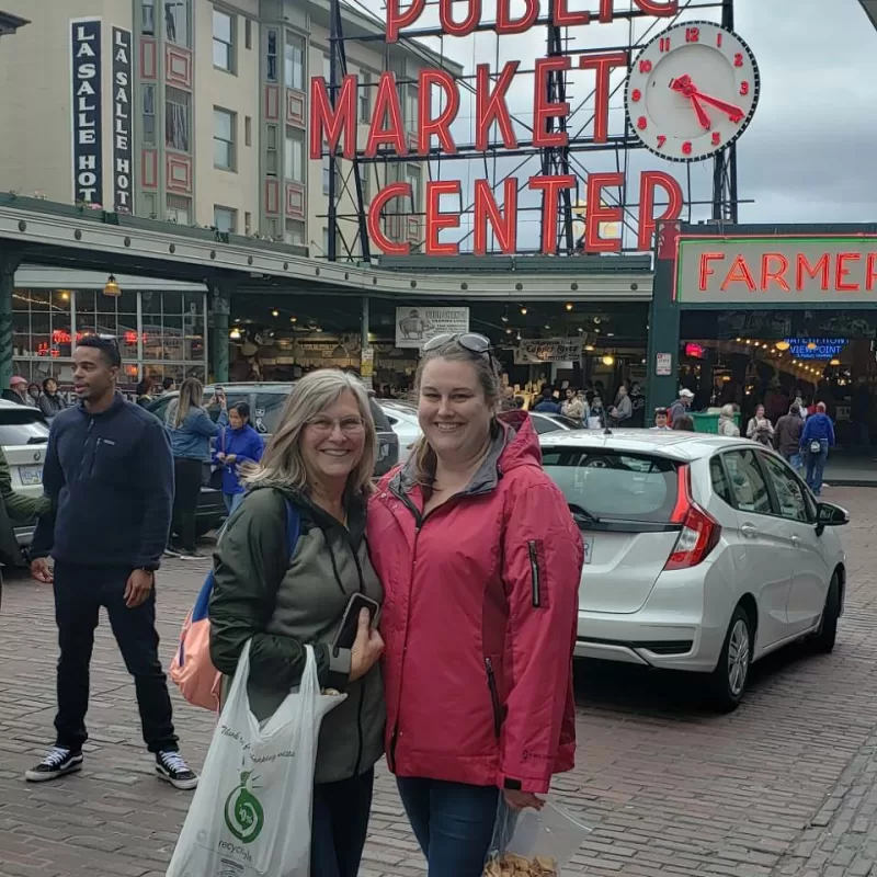 A mother and her adult daughter standing in from of the Public Market Center sign in Seattle, Washington